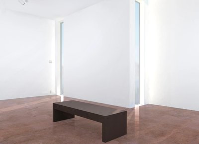The simple architectural style of this gallery imparts scale with a minimum of fuss. It features floor to ceiling windows and a simple wooden bench on a chocolate tinted stone floor.